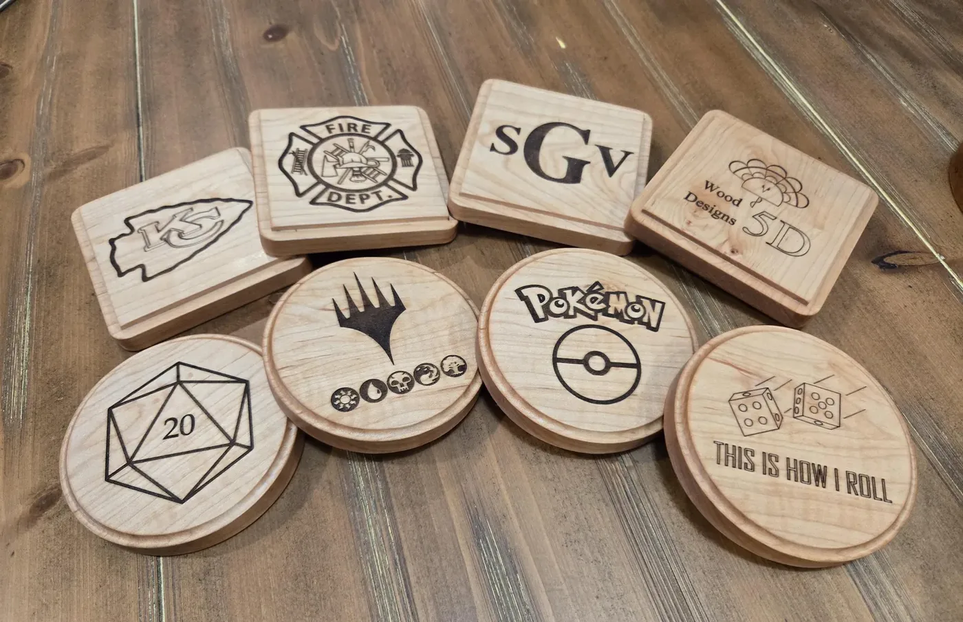 Assorted custom engraved wooden coasters laid out on a wood table